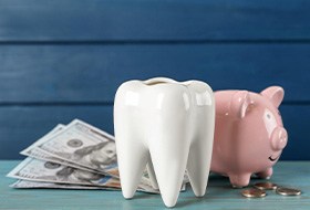 Dollar bills, a piggy bank, a large ceramic tooth, and coins on a table