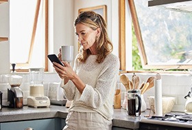 Woman looking at her phone while drinking coffee in the kitchen