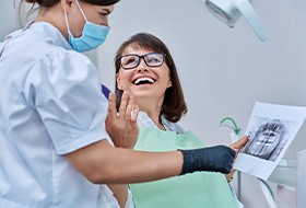 Woman smiling with dentist while reviewing X-ray