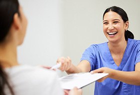 A dental hygienist handing dental insurance forms to a patient