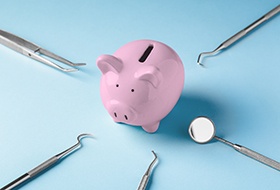 A pink piggy bank surrounded by dental tools