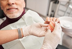 Dentist’s gloved hands handing dentures to patient in dental chair