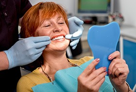 Woman with red hair in dental chair smiling at her reflection with dentist touching the corners of her mouth