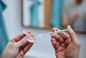 Hands squeezing teeth whitening gel into clear applicator tray