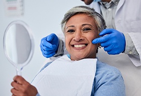 Woman smiling while holding handheld mirror with dentist