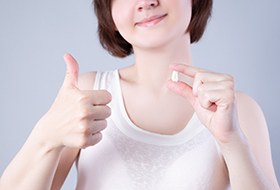 Nose-to-chest view of woman holding extracted tooth and giving thumbs up
