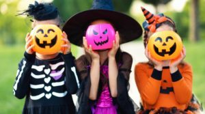 three little kids holding plastic jack-o-lanterns in front of their faces 