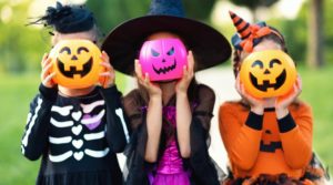 three little kids holding plastic jack-o-lanterns in front of their faces