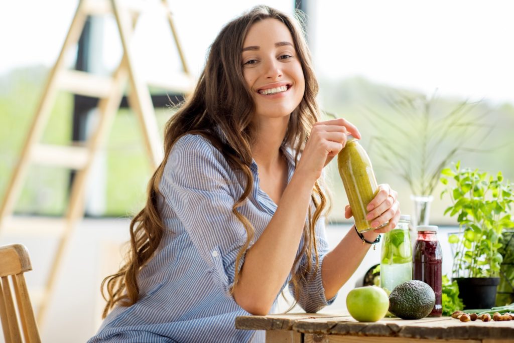 Woman with veneers smiling while drinking green juice