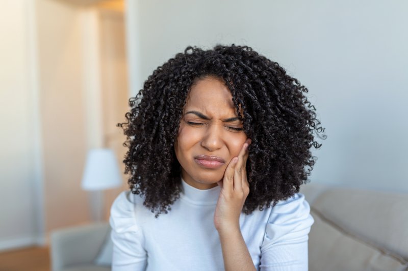 Woman holds cheek in pain.