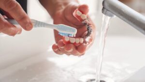 Hands brushing partial dentures under running water